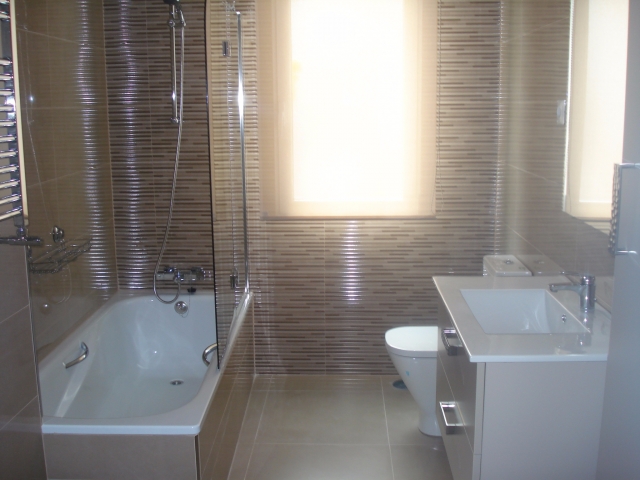 Baño moderno con bañera y azulejos oscuros reformado por ABC Decoración y Reformas.