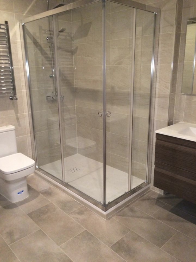 Ducha de cristal en baño renovado con acabados texturizados por ABC Decoración y Reformas.